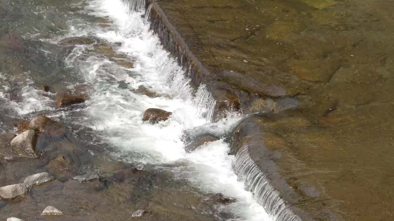 Een statische opname vanuit een hoog standpunt toont vers water dat stroomt over een kleine rotsachtige rivierwaterval.