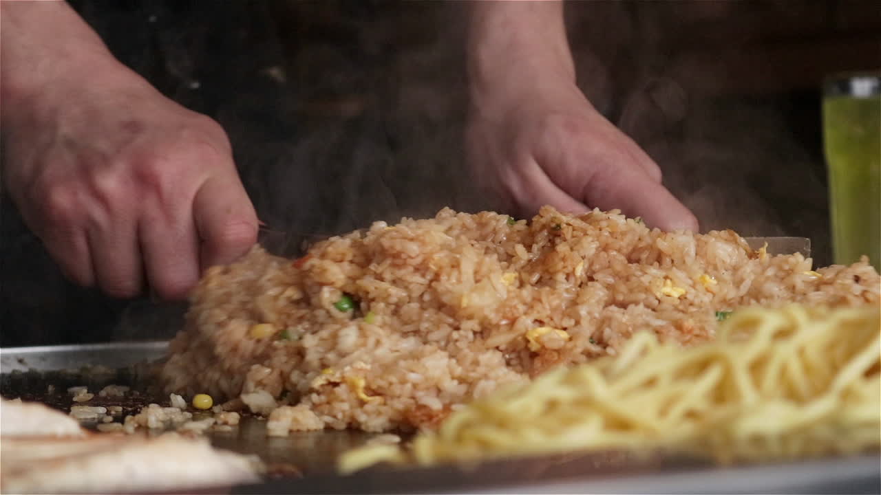 Slow motion close up of a Japanese chef preparing fried rice on a flat top teppanyaki grill