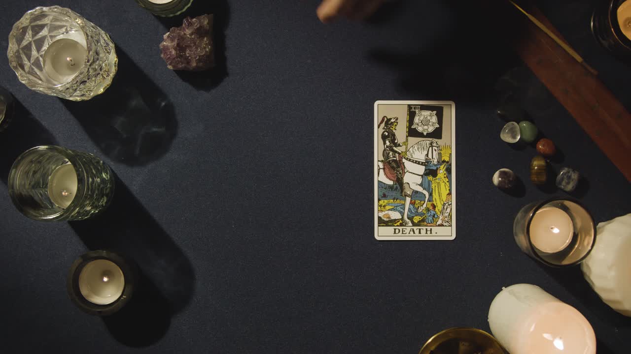 disparo desde arriba de una persona que da lectura de cartas del tarot colocando la carta de la muerte en la mesa