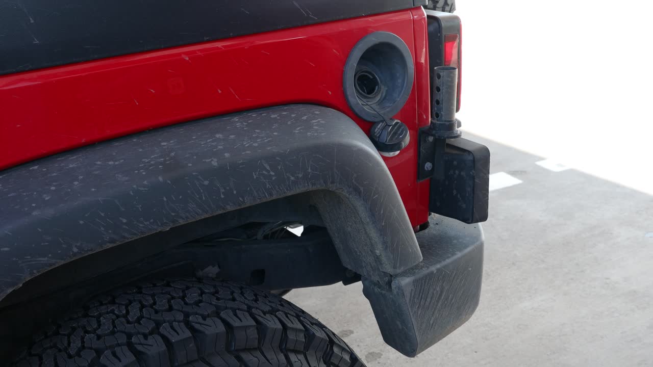 mujer quitando la boquilla de gas de su camioneta roja en la gasolinera