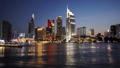 a static timelapse of saigon’s skyline as it shifts from sunset to night, with buildings lighting up and shimmering reflections on the river