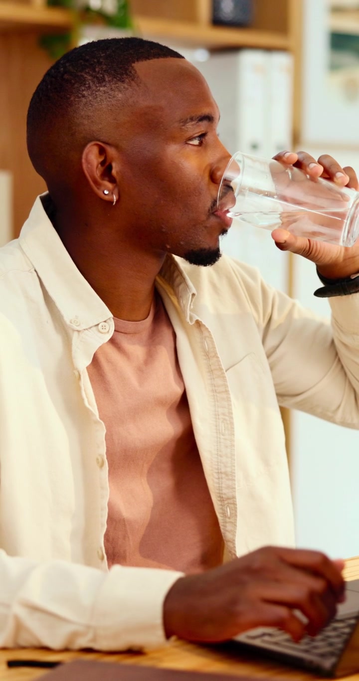Young Man Working on Laptop and Drinking Water in Office