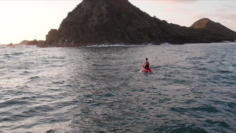 vista trasera de un dron cinematográfico de un hombre solitario remando en un kayak rojo hacia las islas hawaianas de na mokulua