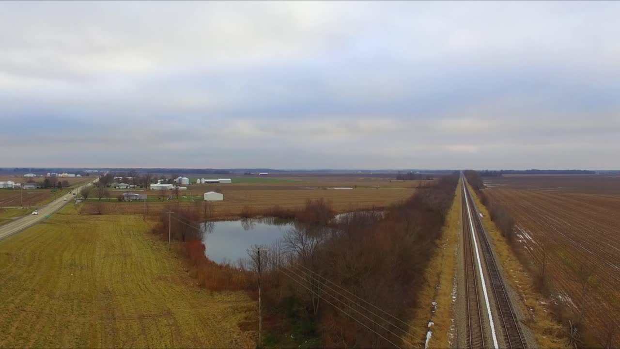 automóviles, camiones y un autobús que viajan a través de un paso elevado que pasa sobre las vías del tren junto a un estanque en una carretera rural de illinois