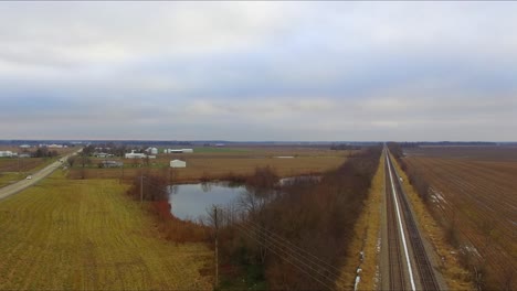 automóviles, camiones y un autobús que viajan a través de un paso elevado que pasa sobre las vías del tren junto a un estanque en una carretera rural de illinois