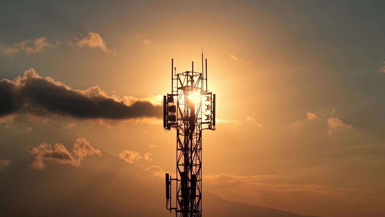 Cell phone signal tower silhouetted at sunset with clouds. Telecommunication, connectivity, and network infrastructure concept footage.