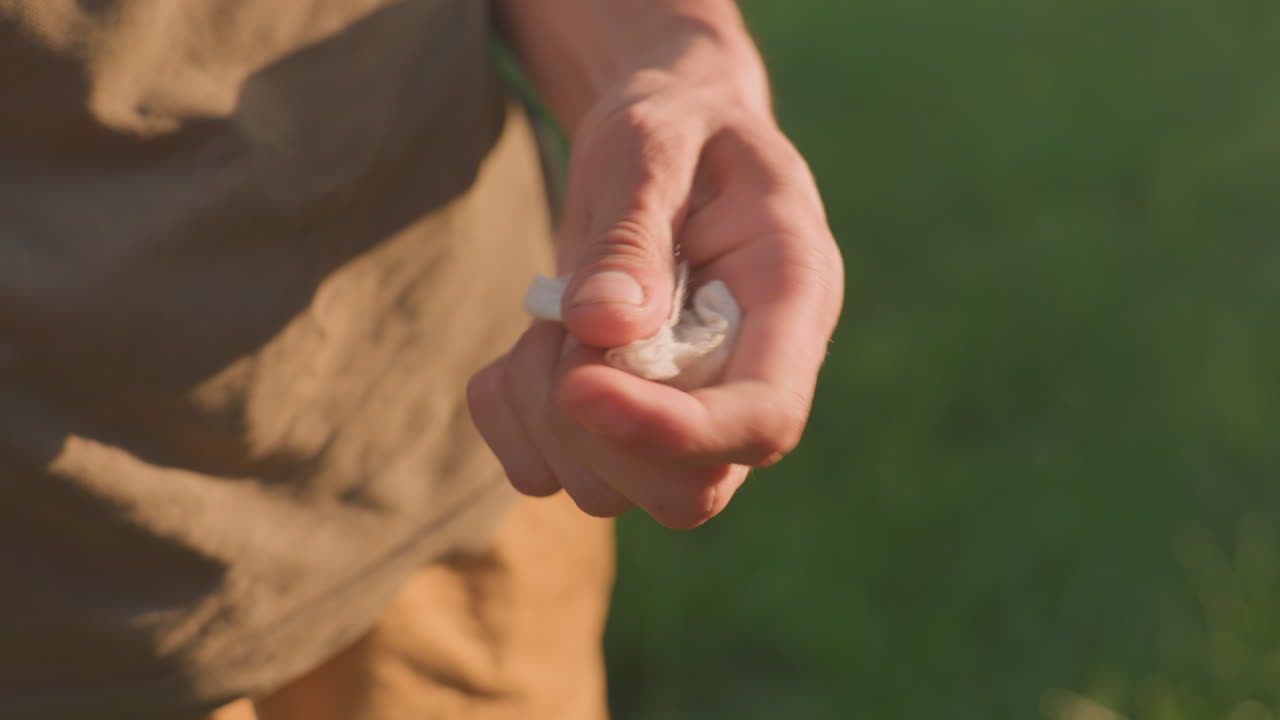 Stress Response Involving Tissue Gripping, Person Displaying Compulsive Tissue Squeezing Under Sunlight, An Individual Exhibits Nervous Habit Of Squeezing Tissue In Sunlit Park Setting