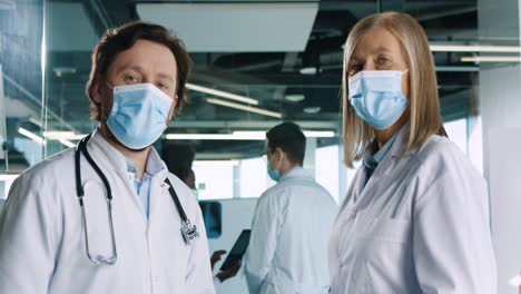 caucasian male and female doctors in medical masks looking at camera in hospital office