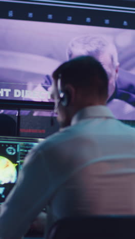 vertical shot of male operator browsing data on computer while watching online broadcast with astronaut on orbital station