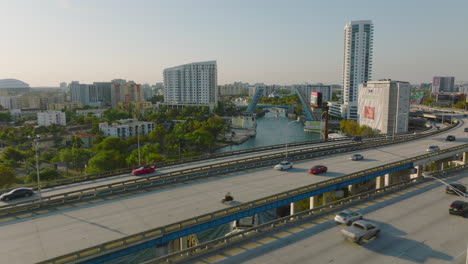 Forwards-fly-above-busy-multilane-highway-in-city.-Revealing-luxury-yacht-passing-on-river-and-heading-to-lifted-bridge.-Miami,-USA