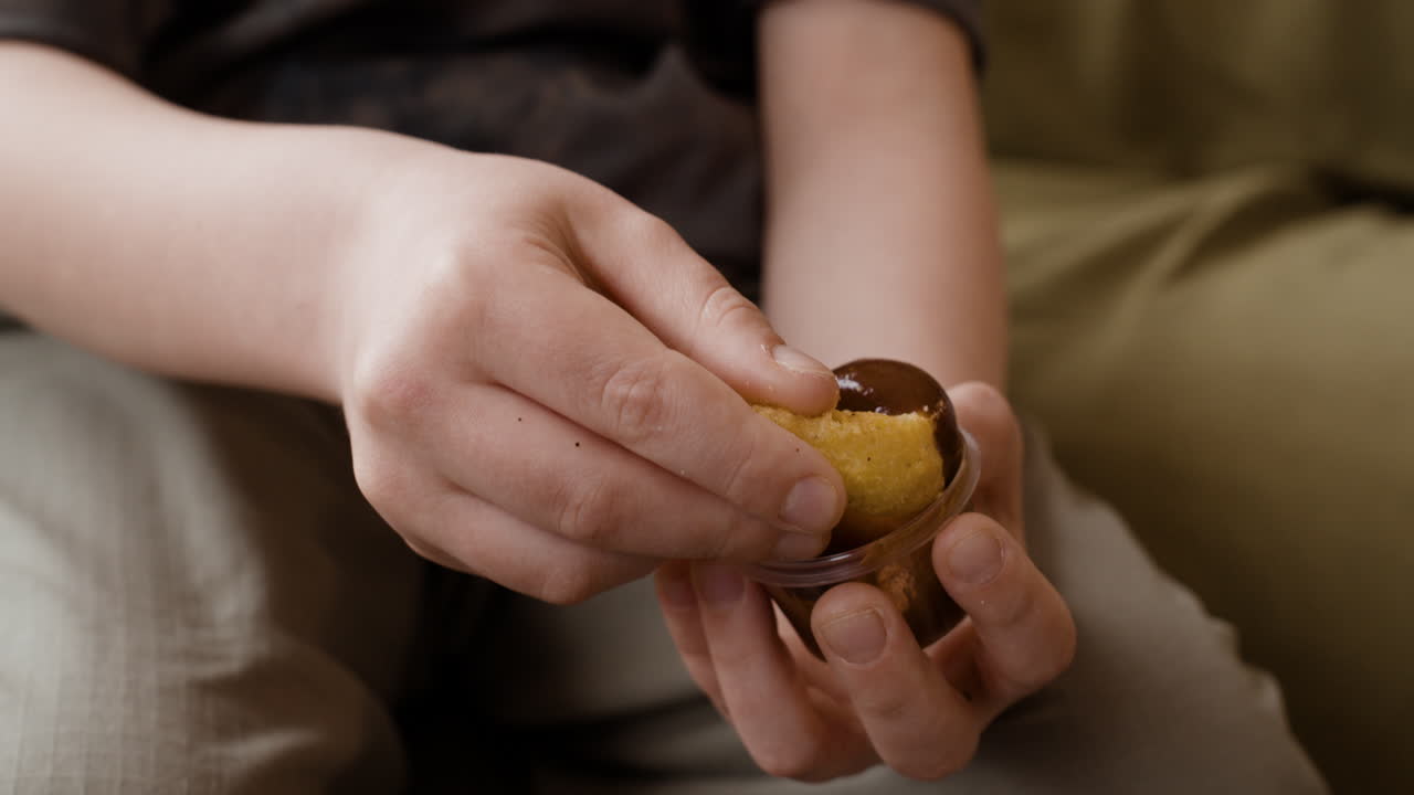 Close-up of hands dipping a snack into chocolate sauce