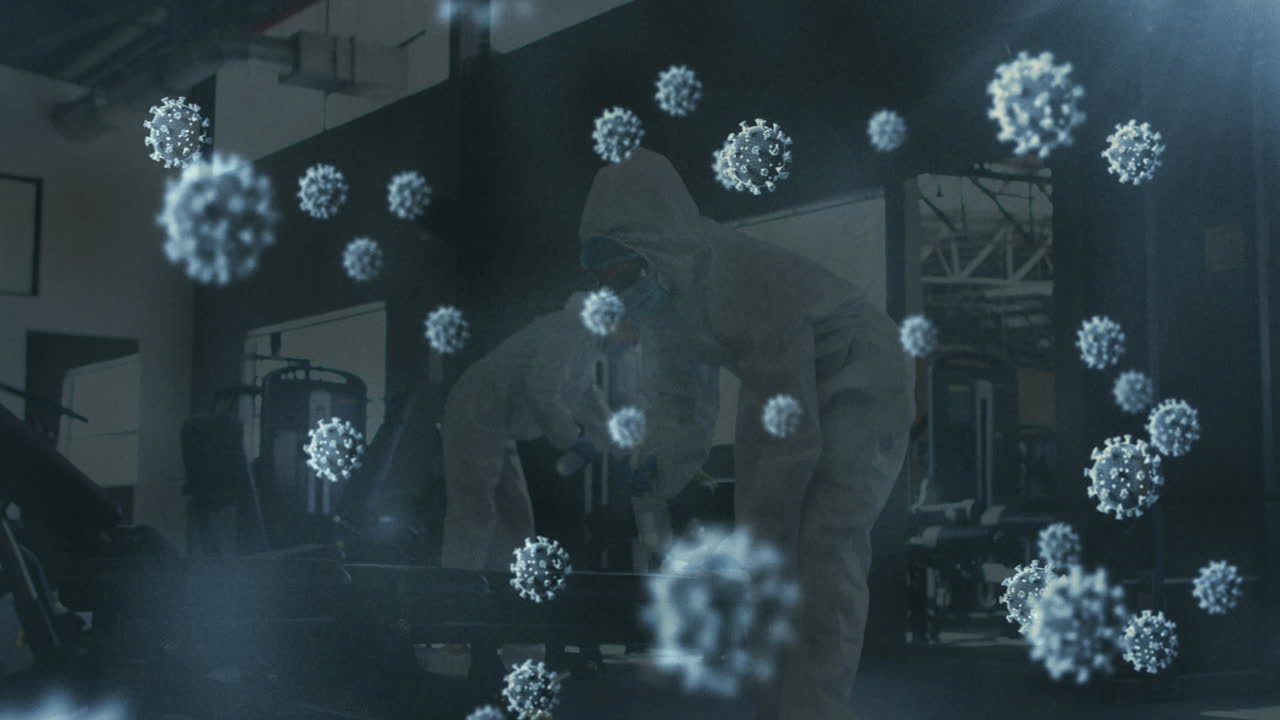 여러 개의 코로나19 세포가 소독제를 사용하여 체육관을 청소하는 보건 노동자 그룹 위에 떠다니고 있습니다.