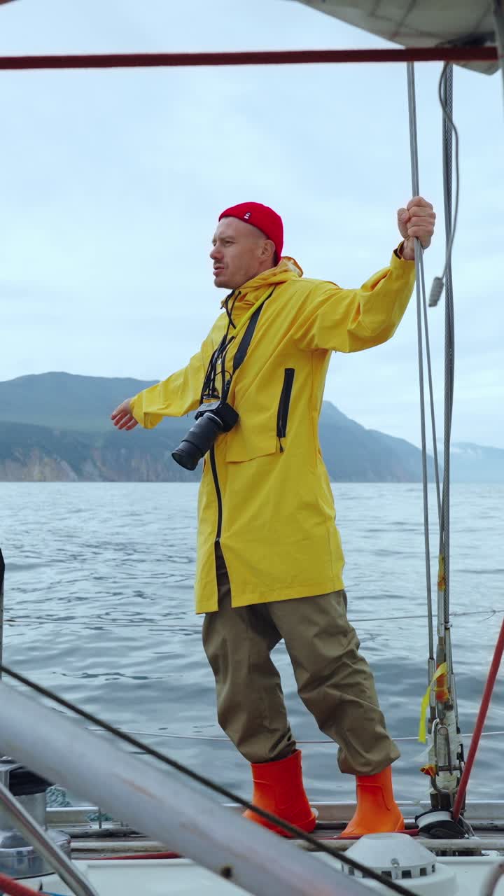 Abenteuerlustiger Mann in gelbem Regenmantel auf Segelboot auf See