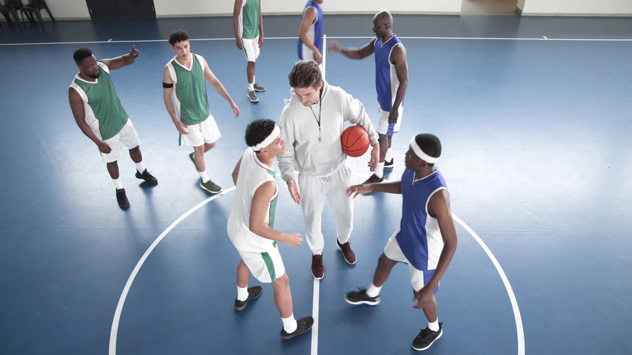 Basketball players preparing for tip-off on indoor court, coach supervising game