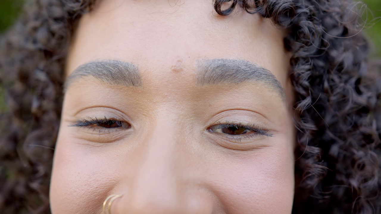 Close-up of woman face with curly hair and nose ring, smiling gently