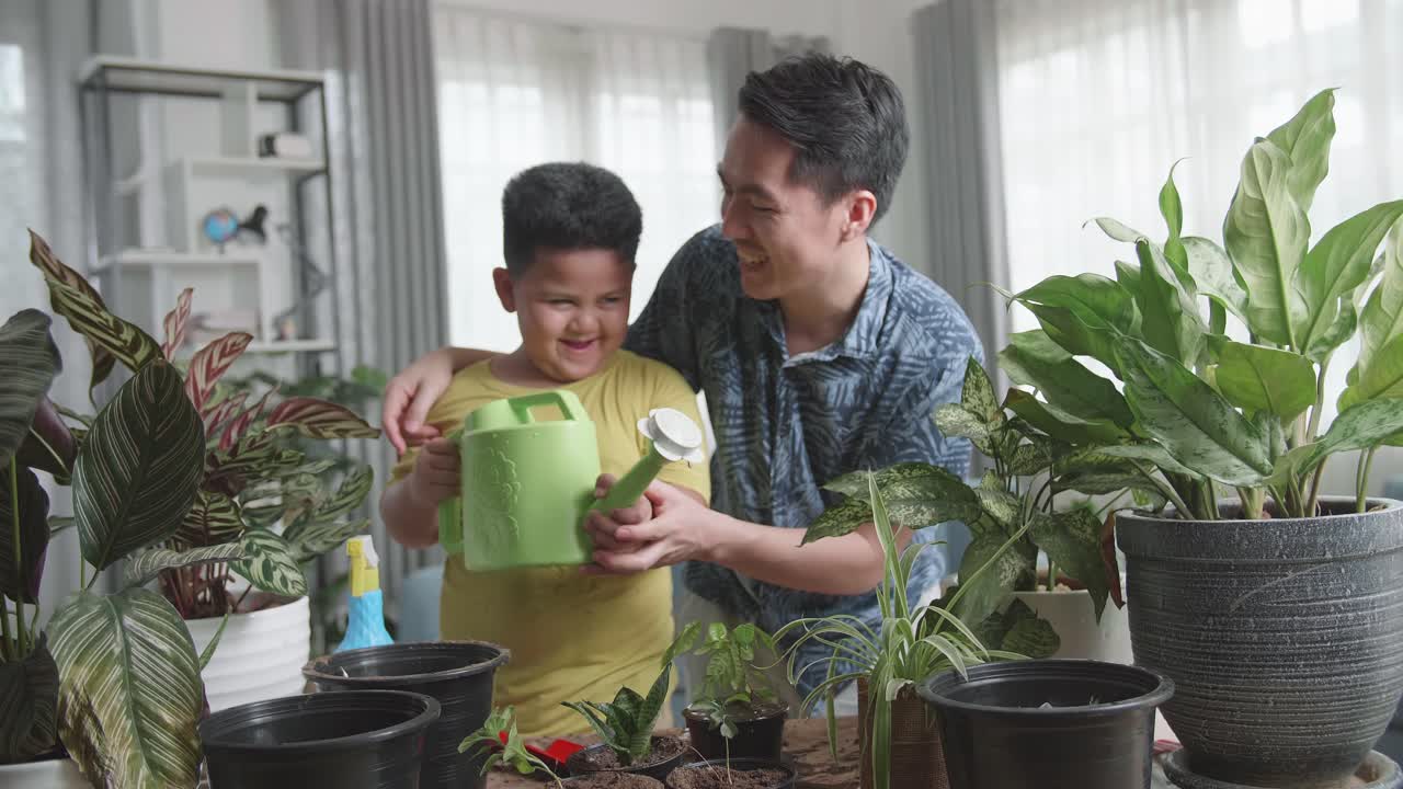 Father And Son Watering Home Plants At Wooden Table Indoors
