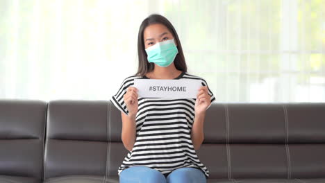 mujer asiática con mascarilla que muestra un mensaje con el hashtag stayhome durante la pandemia de covid-19, cuadro completo