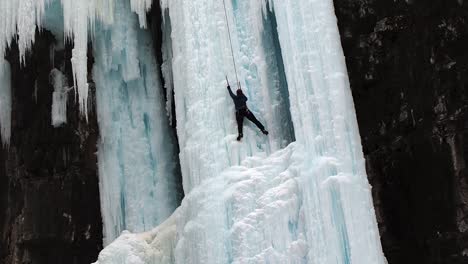 plano medio de una mujer escalando en hielo en una caída de agua congelada