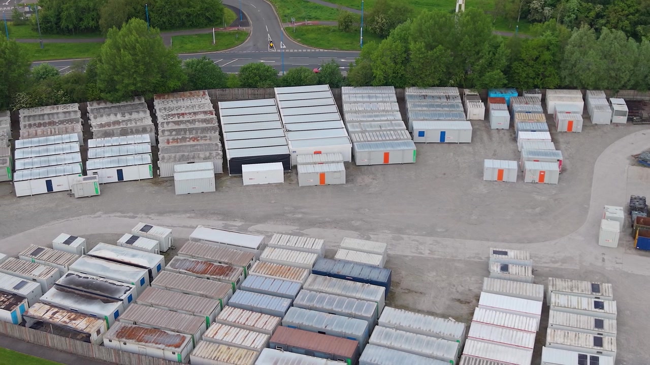 Ripresa aerea laterale di container di spedizione immagazzinati in un deposito industriale. Pile organizzate di carico in acciaio. Scorte in eccesso, gestione della logistica, vasta scala di soluzioni di stoccaggio industriale. Regno Unito