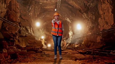 full body of asian female engineer with safety helmet smiling and touching her chest then pointing at you in underground mine tunnel