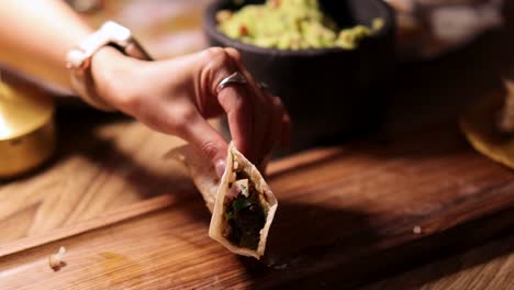 a hand places a taco on a wooden board, surrounded by vibrant ingredients in a warmly lit restaurant setting