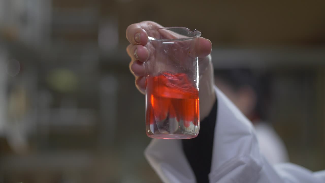 científico sosteniendo un vaso con líquido rojo