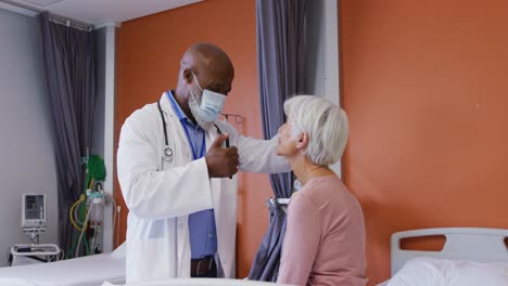 African-american-male-doctor-using-penlight-examining-the-eyes-of-senior-caucasian-female-patient