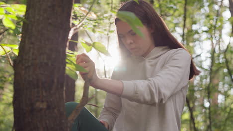 una mujer utiliza una rama de árbol para estirar la pierna levantada en el bosque. una mujer concentrada realiza ejercicios de estiramiento para aliviar la tensión en las piernas después de correr en un día soleado