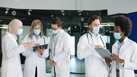 multiethnic doctors team in medical mask discussing coronavirus infection while typing on tablet in hospital