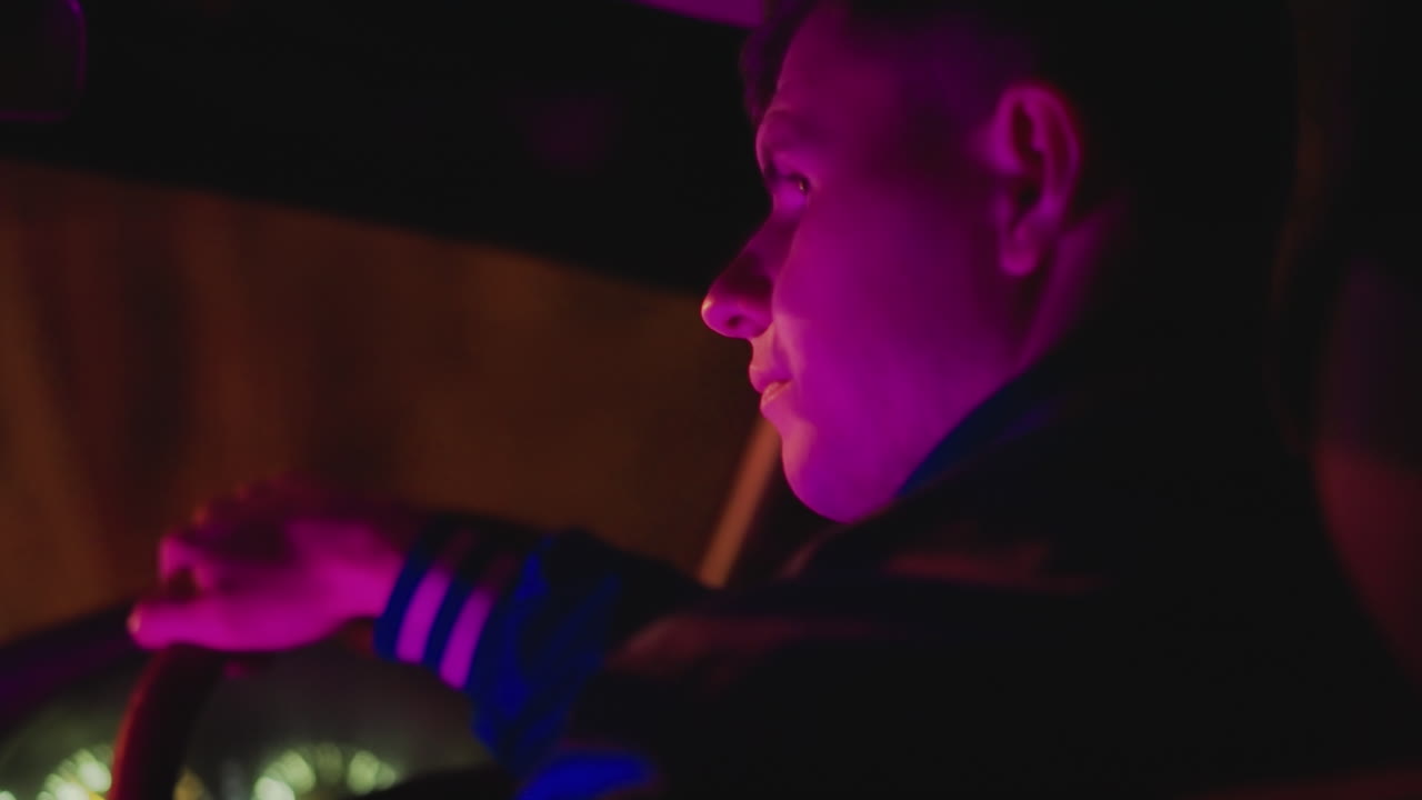 Kuljettajan sivukuva neonvalossa, tarkistamassa kaistaa ja taustapeiliä ohjatessaan rauhallisia kaupunkikatuja kyytipalvelun tunnelmissa, jossa on synkkä violetti sävy, matala syväterävyys ja heijastavuus