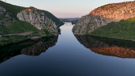 aerial center view of portas de ródão, where the tejo river flows through towering cliffs in vila velha de ródão. a stunning beira baixa landmark with a bridge, perfect water mirror at sunset.