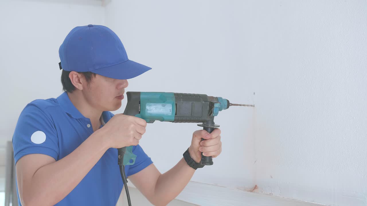アジアの男の技術者 作業員が家で壁に電気ドリルを使っています 家の改良と修理