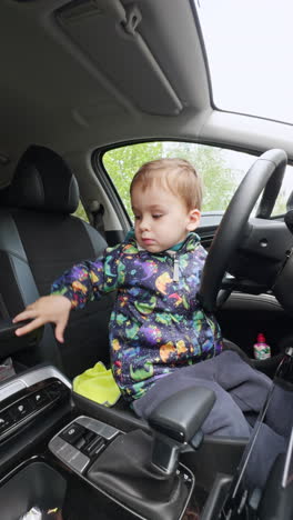 lovely baby boy in warm jacket cleaning inside the dad's car. kid uses the yellow rag dusting the panels. vertical video.