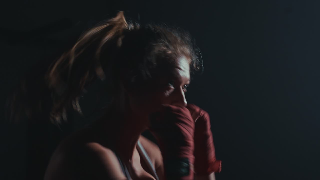 Donna determinata che pratica shadow boxing in una palestra buia con illuminazione drammatica