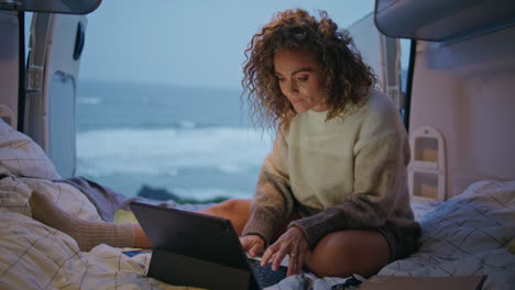 remote worker surfing camper van looking laptop at evening. woman freelancer