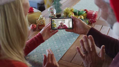 Kaukasisches-Paar-Mit-Weihnachtsmützen-Nutzt-Smartphone-Für-Weihnachtsvideoanruf-Mit-Frau-Auf-Dem-Bildschirm