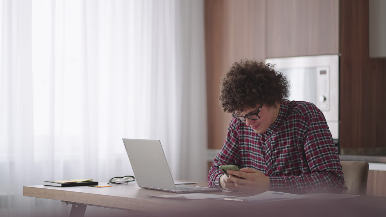 Young man with smartphone in his hands. Modern businessman or student at home office. Freelancer at work. Young student man study at home with laptop and uses a smartphone