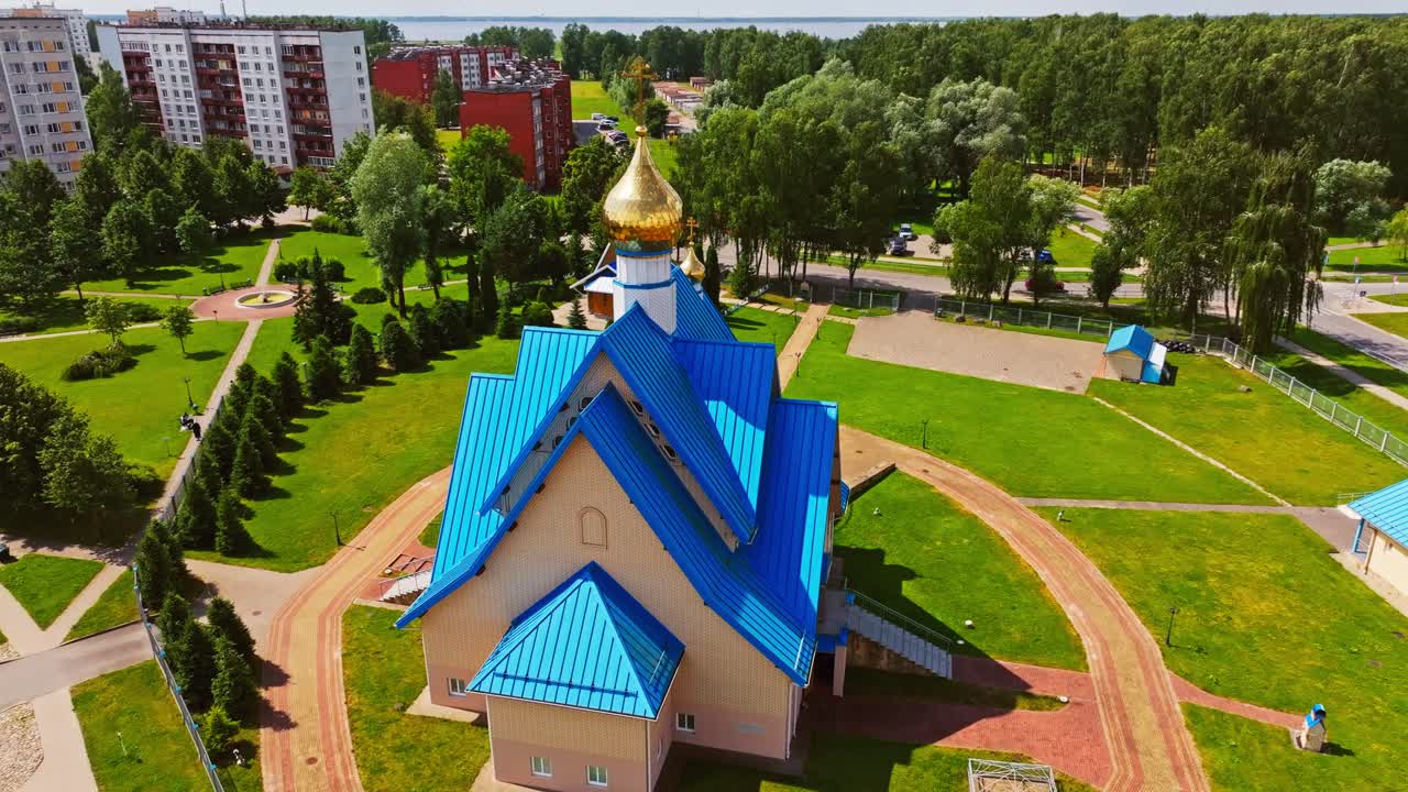 Drone slowly circles church with golden domes, vivid blue roofs amid city block