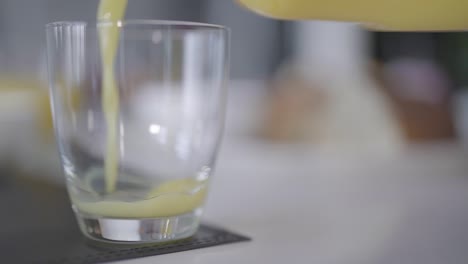 orange juice is poured into a glass in slow motion as the camera tracks to the left