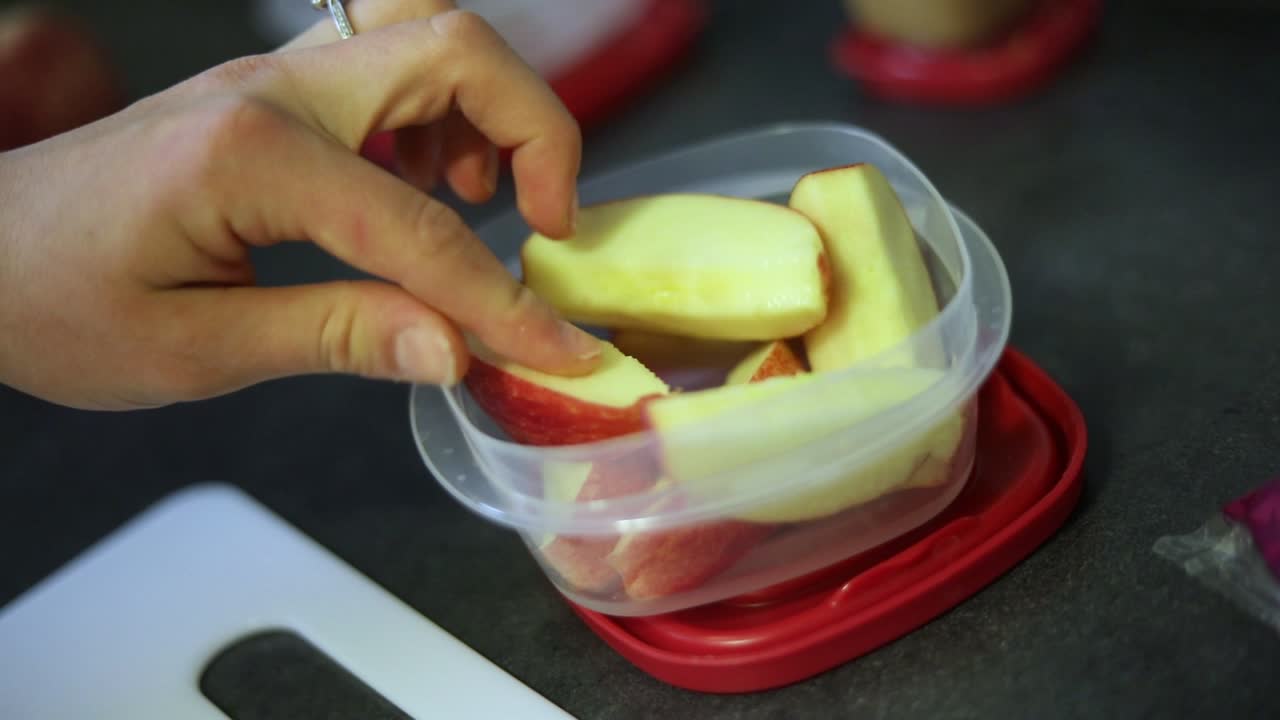toma en cámara lenta de alguien poniendo rodajas de manzana recién cortadas en un pequeño recipiente de tupperware