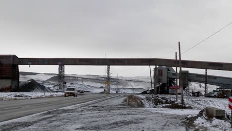 Pan-across-an-old-abandoned-mine-in-winter-with-traffic-passing-on-a-road