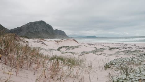 Unberührter-Strand-Mit-Sanddünen-Und-Vegetation,-Während-Sich-Die-Wellen-Brechen-Und-Berge-In-Der-Ferne