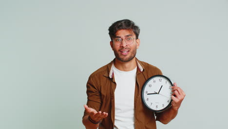 indian young man with anxiety checking time on clock, running late to work, being in delay, deadline