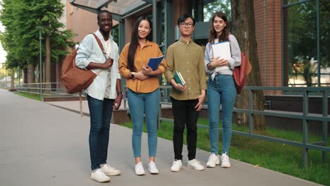 full lenght view of a group of multiethnic students looking at camera and smiling in the street near the college