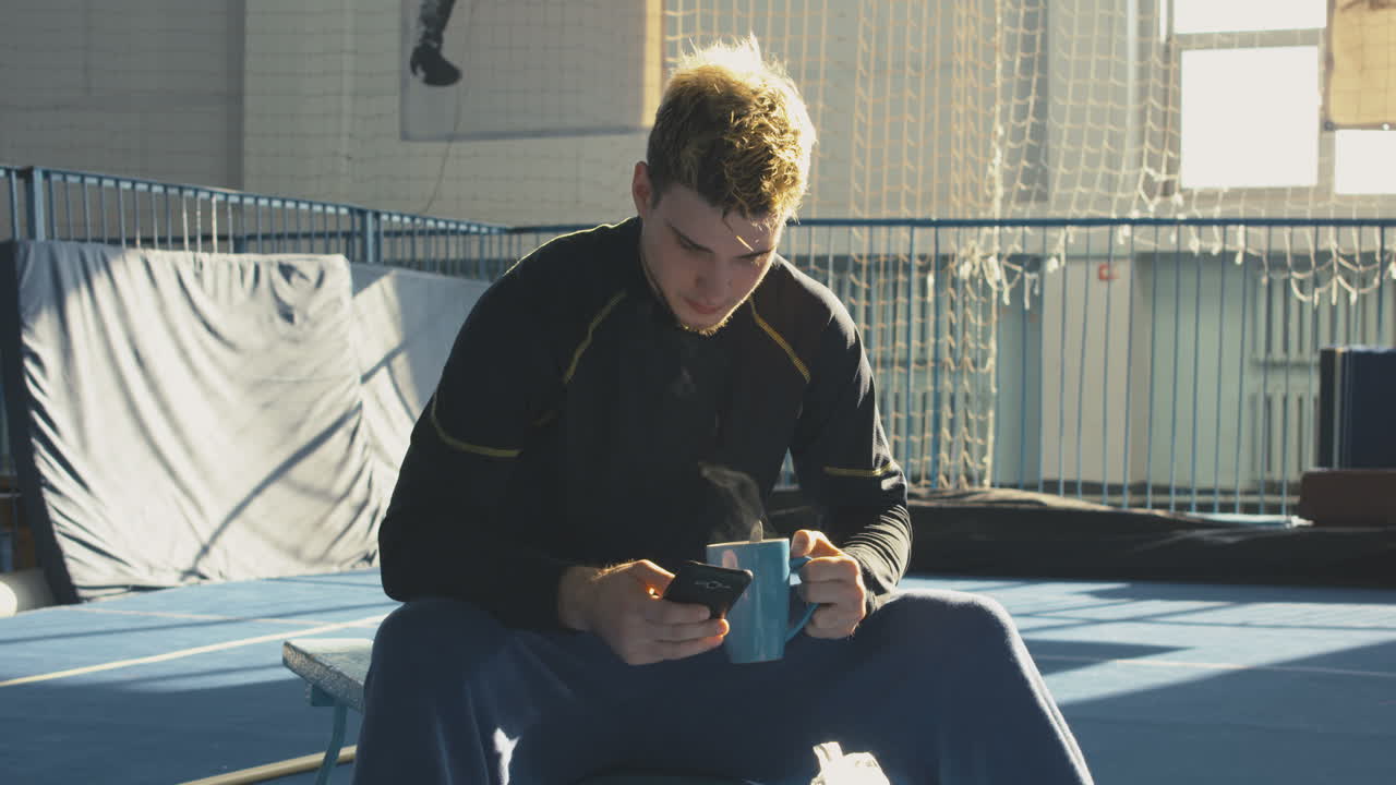 Man Relaxing with Coffee and Phone in a Gym