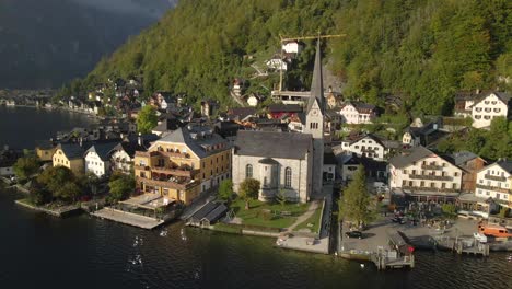 Hallstatt-town-center-with-picturesque-evangelical-Pfarrkirche-church-during-sunrise,-aerial