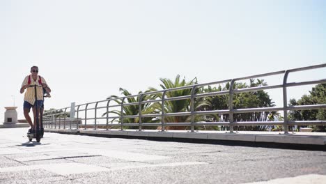 happy diverse gay male couple using scooters at promenade by the sea, slow motion