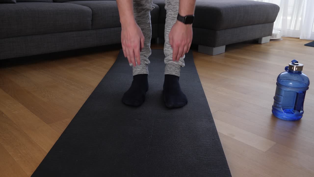 Leg view of a male athlete doing stretching exercises on a sports mat in the living room
