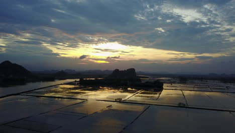 witness a stunning tilt-down view of a flooded area with rice plantations in ninh binh, vietnam, during a vibrant sunset. the scene captures the serene beauty and unique agricultural landscape.
