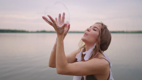 a young girl artist shows magic tricks using soap bubbles. create soap bubbles in your hands and inflate them location theatrical circus show at sunset